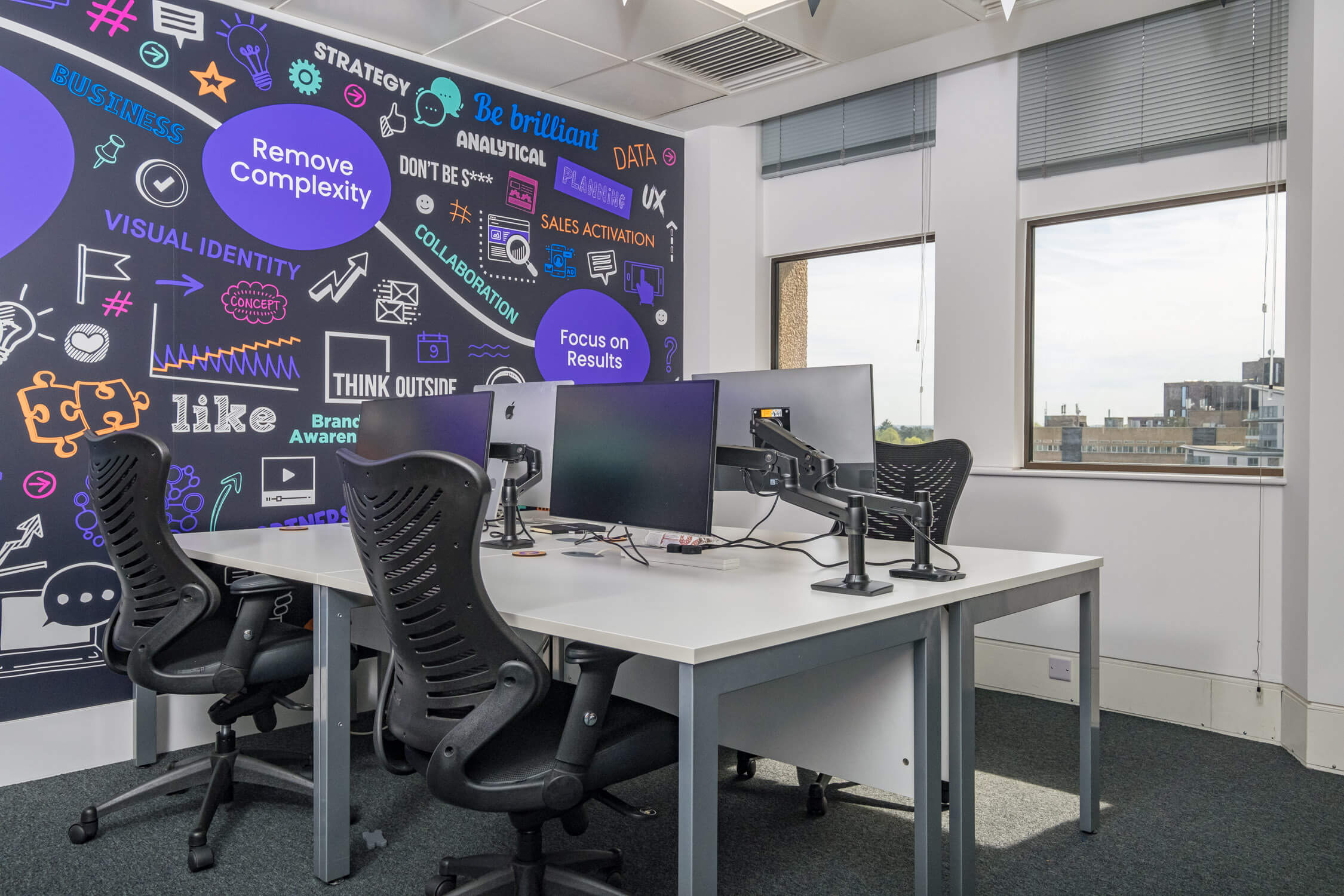 A closeup of four desks and chairs in an office. These desks and chairs are setup with four screens.