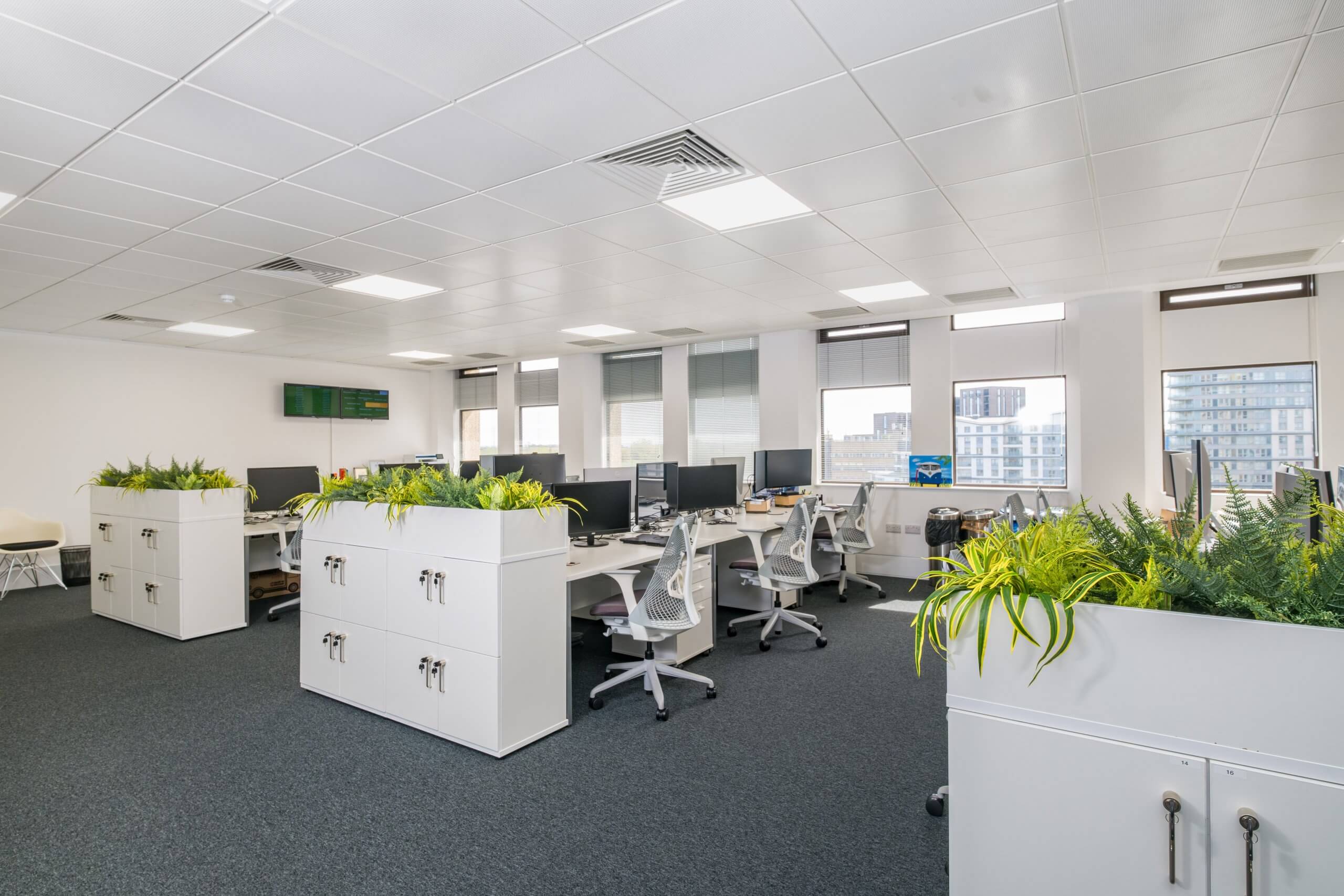 Large office with three separate rows of white desks and chairs.