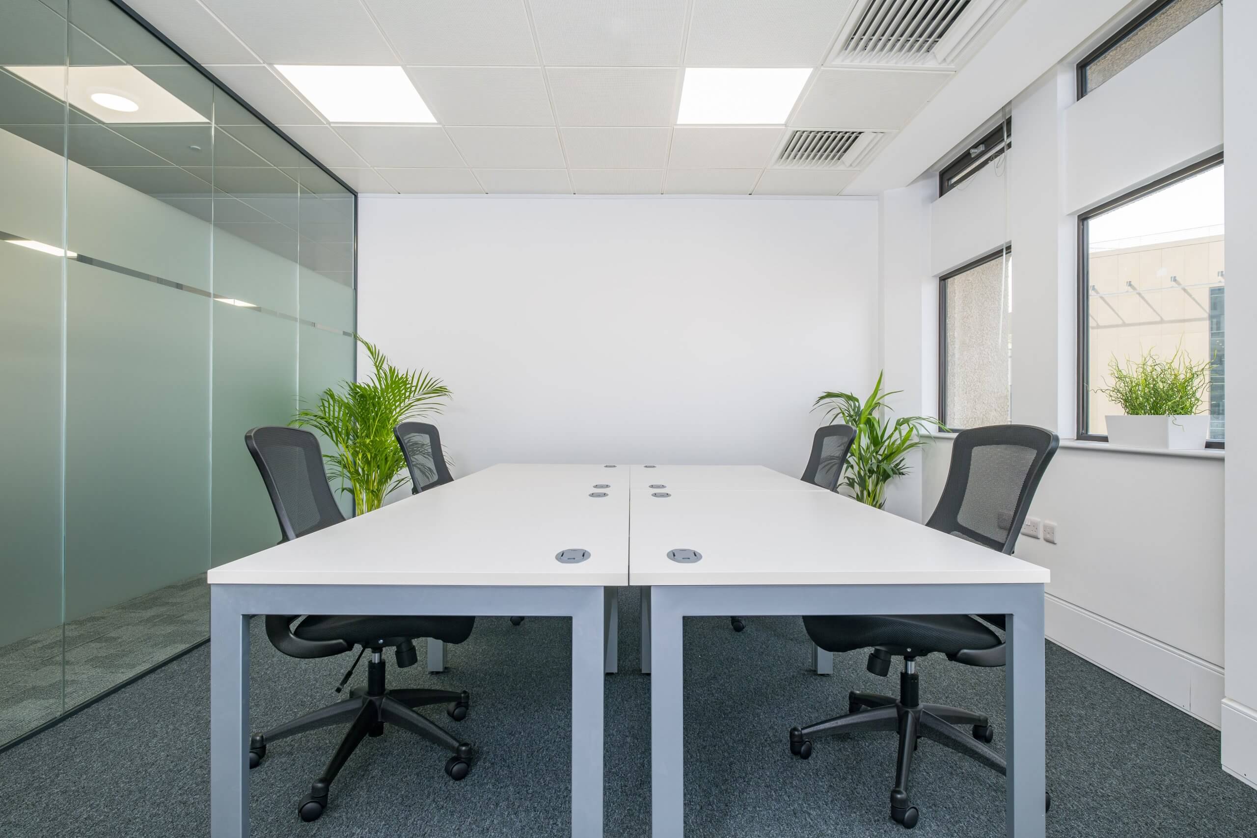 Small office with four white desks and black chairs in the middle of the room.